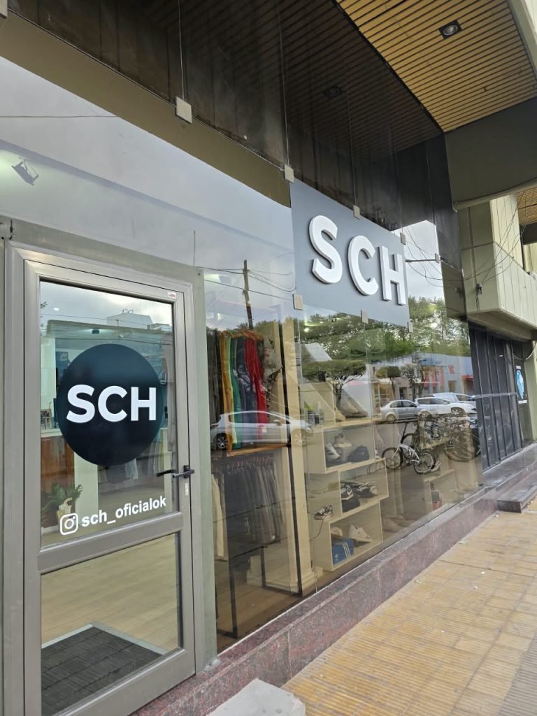 Frente del local SCH: puerta de vidrio con el sticker negro de SCH y el usuario de Instagram, y cartel con letras blancas sobre gris