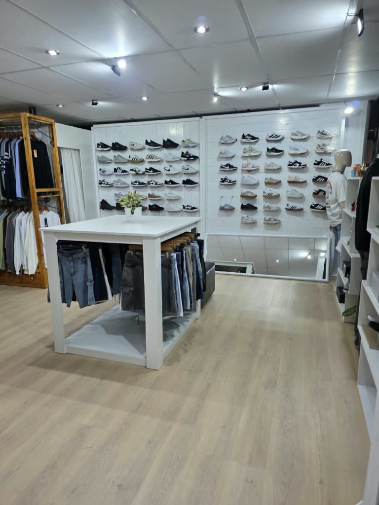Interior del local SCH: pared blanca llena de zapatillas en repisas, mesa blanca con jeans colgados y perchero de madera con ropa