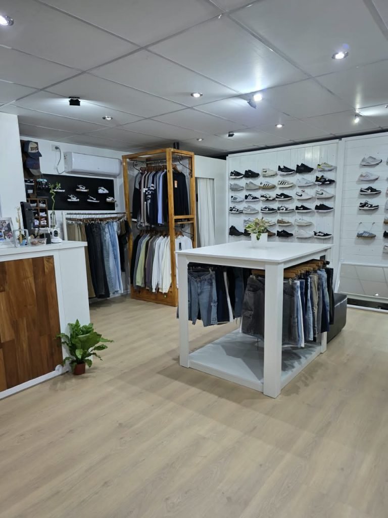 Interior del local SCH visto desde la entrada: mostrador de madera, percheros con ropa y la pared de zapatillas al fondo