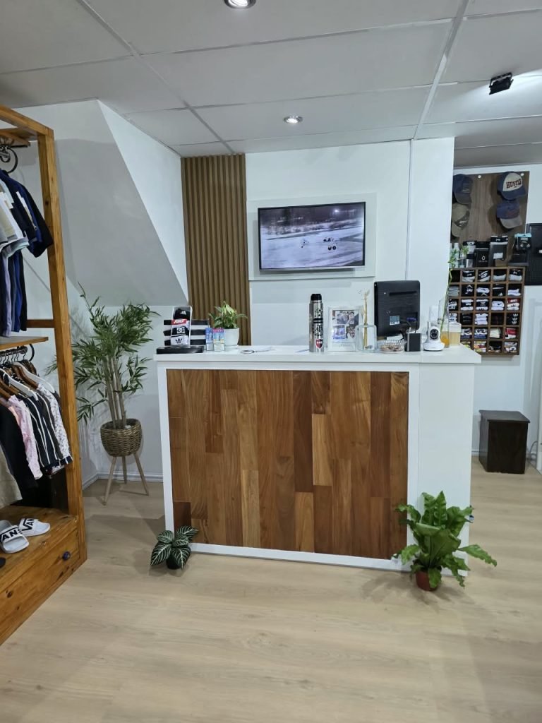 Mostrador del local SCH con frente de madera, plantas y gorras en la pared