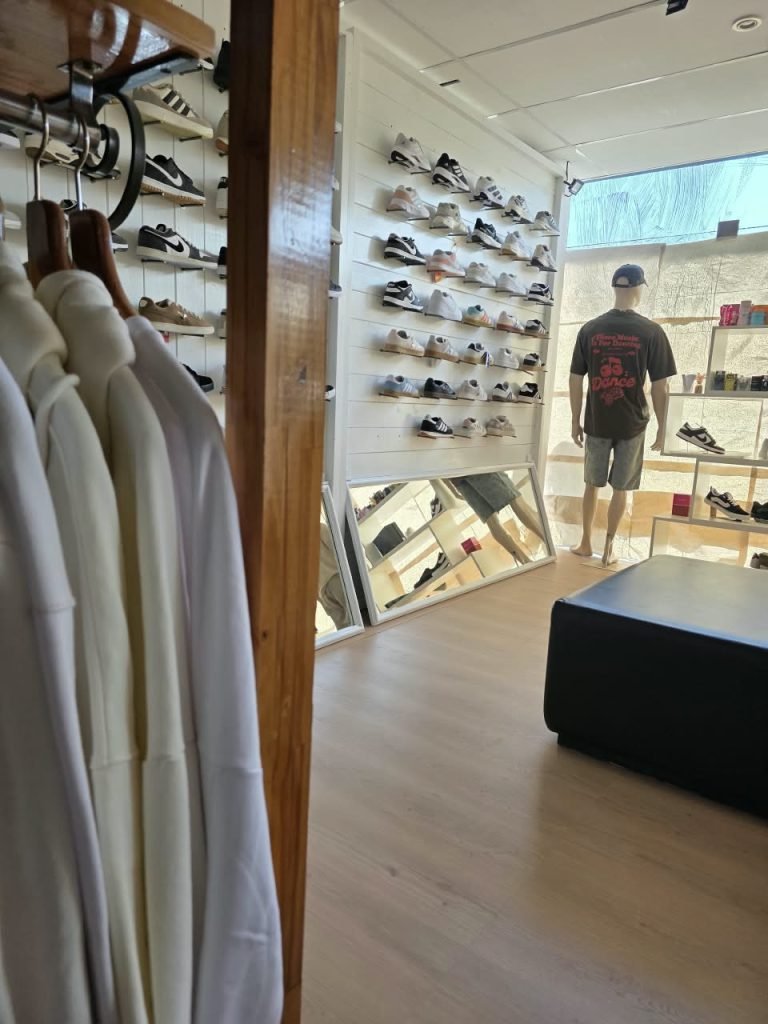 Interior del local SCH: buzos claros colgados en primer plano y la pared de zapatillas con un maniquí al fondo