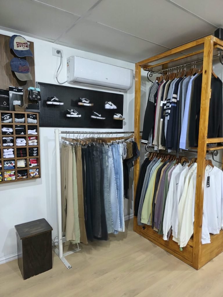 Rincón del local SCH con pantalones y jeans colgados, buzos en el perchero de madera, medias y gorras