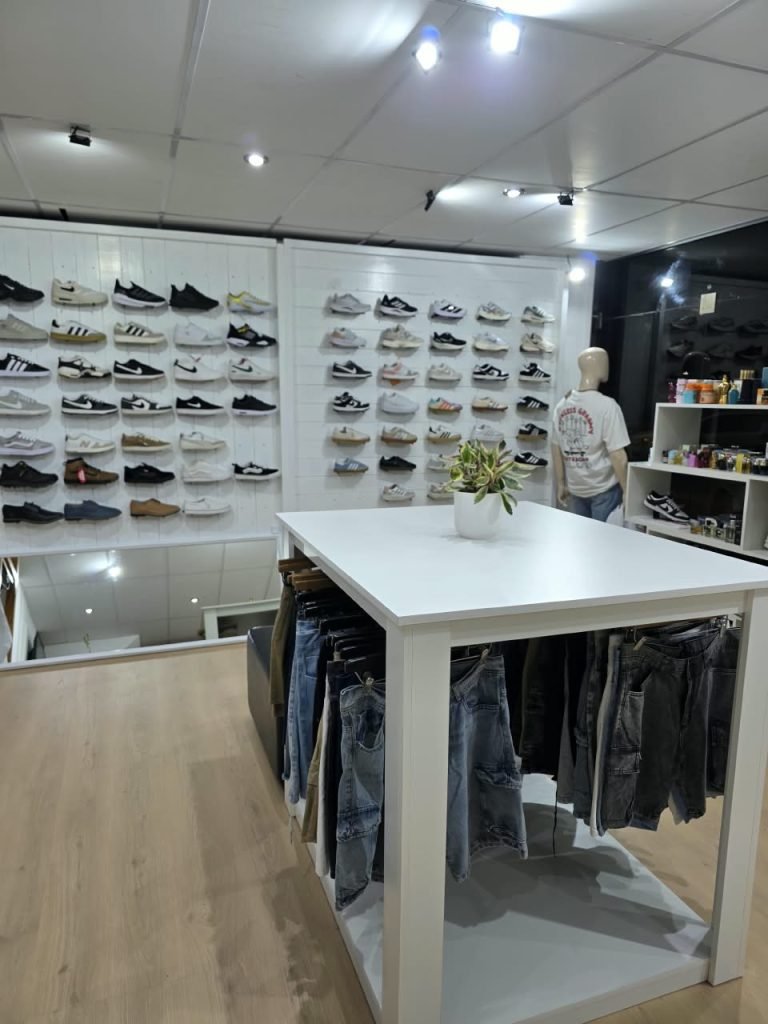 Pared blanca de listones con zapatillas en repisas y mesa blanca con jeans colgados en el local SCH